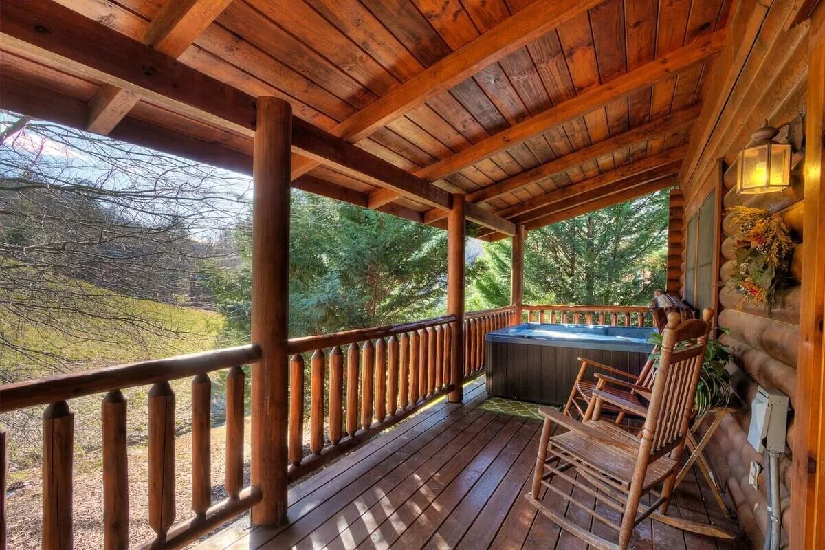 In this image, the deck features both a hot tub and a pair of classic rocking chairs, set against natural greenery and a wooden railing. The setup suggests a harmonious blend of relaxation options—whether soaking in the tub or enjoying a quiet moment in the chairs.